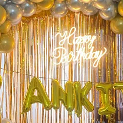 A glamorous gold-themed birthday backdrop. This setup features a shimmering gold foil curtain, a "Happy Birthday" neon sign, and the name "ANKIT" in large gold foil balloons, perfect for a milestone celebration.