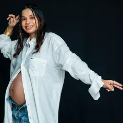 A confident and modern maternity portrait. The mom-to-be rocks a casual, unbuttoned white shirt and jeans, showing off her bump with style and attitude.