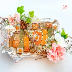 This hamper showcases a diverse assortment of gourmet mithai on an elegant silver-plated tray. I love combining different colors, textures, and flavors, all brought together with a delicate floral and twig arrangement.