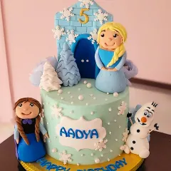 An all-edible "Frozen" theme cake for a 5th birthday. This cake features hand-sculpted figures of Elsa, Anna, and Olaf, complete with an ice castle and snowflakes.