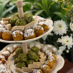 Tradition, served with style. This two tiered stand is filled with classic Indian sweets, including pistachio barfi and motichoor laddoos dusted with silver varq.