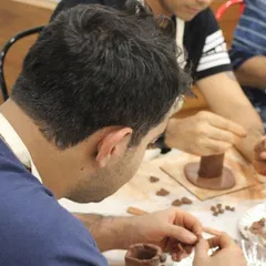 Two men are focused on their clay projects, carefully shaping and adding details to their hand-built pottery pieces.