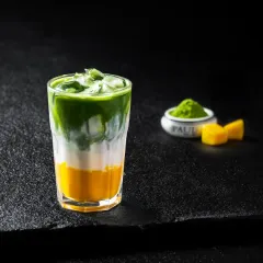 A layered iced matcha drink with a mango base, creating a beautiful gradient of yellow, white, and green.