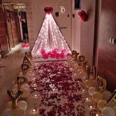 A romantic birthday surprise featuring a canopy tent at the end of a path of rose petals and candles. 'HAPPY BIRTHDAY' foil balloons and a heart-shaped balloon complete this intimate setup.