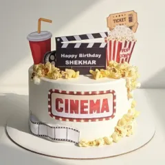 Lights, camera, cake! This cinema-themed cake is a strawberry vanilla flavor, decorated with popcorn, a movie ticket, and a clapperboard for a movie lover's birthday.