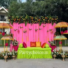 For this outdoor Haldi ceremony, we created a vibrant and festive atmosphere. The setup features a bright pink backdrop, a comfortable lime-green seating area, and decorative Rajasthani umbrellas, all framed by a thick garland of marigolds.