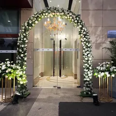 A grand floral arch at the entrance of the Crowne Plaza for a Nikaah ceremony. The arch is covered in white roses and greenery, with a classic chandelier hanging in the center.