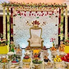 An absolutely divine Seemantham (baby shower) stage, featuring a wall of white flowers, a traditional throne chair, and meticulously arranged offerings. We honour your sacred ceremonies with beauty and respect.