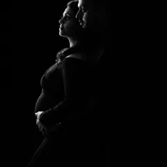 A minimalist and dramatic maternity silhouette. The play of light and shadow beautifully outlines the mother-to-be's form, creating a powerful and artistic black and white portrait.