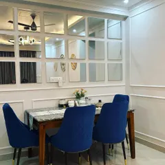 To make this dining area in Jasola feel larger and more glamorous, I designed a custom mirror grid wall. This feature reflects light and the room's decor, creating an illusion of depth. The bold, royal blue velvet chairs add a rich jewel tone that elevates the entire space.