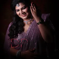 A studio-style portrait with dramatic lighting, highlighting the bride's sparkling purple saree, diamond jewelry, and gentle smile.