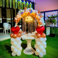 A beautiful outdoor birthday setup on an artificial lawn. The decor includes a balloon ring with a neon sign, heart-shaped foil balloons, and a small table, perfect for a romantic evening.