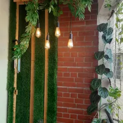 We combined different elements to give this balcony wall a rich, textured look. The exposed brick panel, vertical artificial grass strips, and hanging Edison bulbs come together for a warm, rustic feel.