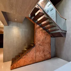 This sculptural staircase is a centerpiece, crafted from copper and metal with cantilevered wooden treads. It embodies a dialogue between lightness and intensity, transforming the act of ascent into a sensory experience, complemented by the natural light from a circular skylight above.