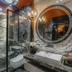 A luxury bathroom in our Vikaspuri project, featuring floor-to-ceiling marble, a large circular mirror with an ornate frame, and a glass-enclosed shower. A classic chandelier adds a touch of opulence.