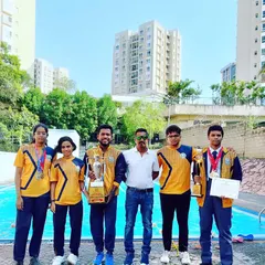 Our team from Ryan Kundalahalli celebrating their National Swimming Championship trophy win, standing proudly with their coach by the pool where they trained.