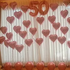 A full wall decoration for a 50th anniversary or birthday, featuring rose gold number balloons surrounded by a cascade of matching heart shaped foil balloons.