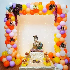 This is a simple yet beautiful decoration for a home Janmashtami puja. I created a colorful balloon frame with small floral details and a backdrop of warm fairy lights to highlight the Bal Krishna idol, making a perfect little mandap at home.