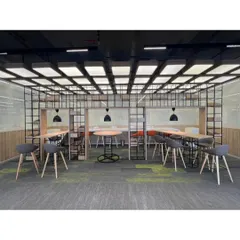 A semi-enclosed collaborative hub within the open office, featuring high tables and stools. The metal grid shelving provides a sense of separation without sacrificing the open feel, making it an ideal space for informal team meetings.