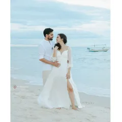 A dreamy pre-wedding portrait on a serene Thailand beach, with the couple dressed in white, standing by the calm sea.