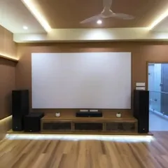 A clean and minimalist living room setup featuring a large fixed-frame screen, floor-standing speakers, and a center channel, all neatly arranged on a modern media console with ambient lighting.