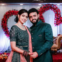 A classic reception portrait. The couple is dressed in elegant matching outfits, posing against a heart-shaped floral backdrop, perfectly capturing the celebratory mood.
