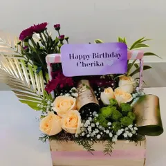 The perfect birthday surprise, this floral basket combines soft peach roses, purple chrysanthemums, and a mini bottle of champagne for a truly celebratory gift. A personalized "Happy Birthday" card completes the arrangement.