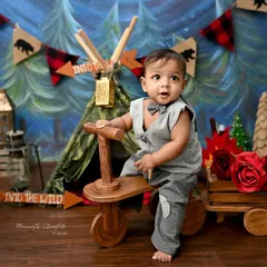 Ready for an adventure in the wild. This little explorer is all set for his camping-themed sitter session, featuring a forest backdrop and a cute wooden tricycle.