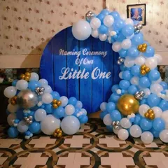 A beautiful Naming Ceremony decoration for a little one. The setup features a deep blue circular backdrop with a wood-panel effect, framed by a blue, white, and gold balloon arch.