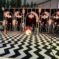 The stage setup for the live band at the 60th birthday bash. The backdrop features elegant white metal arches with chandeliers against a black background, continuing the chic black and white theme.