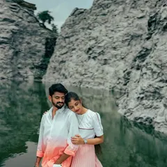 A quiet, intimate moment as a couple embraces by a still lake, with the reflection of the rock face in the water. A peaceful and romantic shot.