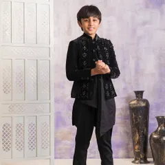 A full view of the black embellished velvet jacket paired with an asymmetrical kurta. This style is a modern take on traditional boys' wedding outfits.
