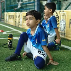 A young player in our toddlers' program sits attentively on the sidelines, learning through observation.