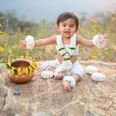 A full, edited shot from an outdoor session. The baby is dressed in a lovely floral outfit, sitting on a rock in a field of wildflowers.