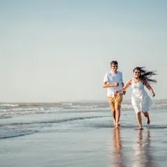Pure, uninhibited joy. A candid shot of a couple running and laughing along the water's edge during their beach pre-wedding session.