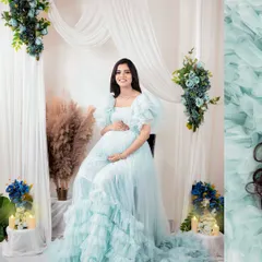 A serene and elegant portrait in a light blue ruffled gown. This setup, with soft white drapes and floral accents, creates a dreamy and peaceful atmosphere.