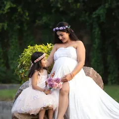 An outdoor maternity portrait with the older daughter, both wearing coordinating floral crowns. Outdoor settings provide a soft, natural light for these special family moments.