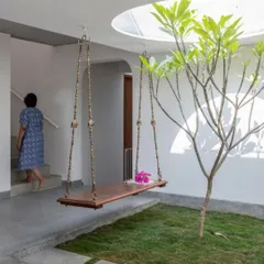 A resident ascends the stairs next to the central courtyard, showcasing how daily life circulates around this natural feature. The design ensures that movement through the house is always connected to light and greenery.