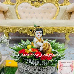 A platter designed for a Krishna Jayanti celebration or pooja, featuring a beautiful idol of little Krishna, surrounded by flowers and leaves.