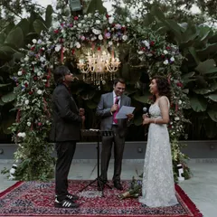 An outdoor wedding ceremony with the couple exchanging vows under a lush floral arch with a sparkling chandelier. This setup combines natural beauty with elegant design.