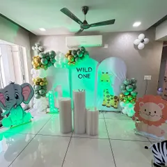 A "Wild One" jungle-themed birthday decoration designed for a home space. This setup uses arched backdrop panels with animal prints, character cutouts of an elephant and lion, and green-toned lighting to create a jungle vibe.