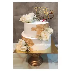 An elegant two-tier "Bride to be" cake. The design features a modern gold brushstroke effect on white buttercream, adorned with fresh white roses and a custom topper.