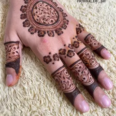 A beautiful mandala design on the back of the hand, featuring a central floral pattern with a vine-like fill. The fingers are decorated with matching bands and small flowers.