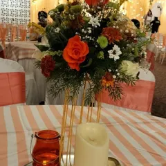 This table centerpiece combines a vibrant floral arrangement with a modern gold-wire vase and candle lighting. The striped tablecloth and colored glass add layers of texture and color to the overall design.