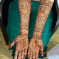 This bridal design is filled with traditional elements, including elephant motifs, hanging bells (jhumkis), and detailed portraits, telling a complete story on the arms.
