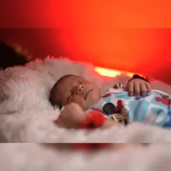 A peaceful close-up of a sleeping newborn. The warm red-orange light in the background adds a beautiful, soft glow to this serene portrait.