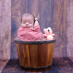 A classic newborn pose, with the baby swaddled and sleeping soundly in a rustic wooden bucket. This highlights their tiny, curled-up form perfectly.