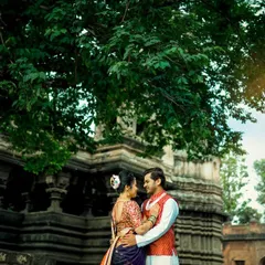 A beautiful portrait of a couple in traditional outfits, standing together under a large tree with an ancient temple structure in the background. A perfect blend of love and heritage.