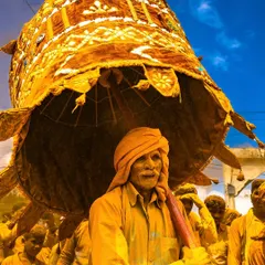 A devotee carries a large, decorated umbrella during the Vittal Birdev Yatra in Pattan Kodoli. The entire scene is drenched in golden turmeric powder, creating a surreal and vibrant atmosphere.