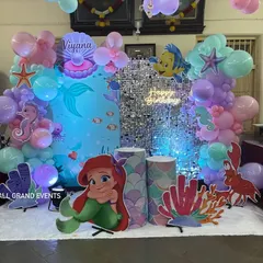 A close-up of the mermaid-themed stage, highlighting the pastel balloon arch and life-sized cutouts of Ariel, Sebastian, and a seahorse.